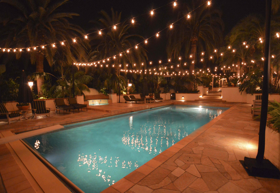 A gorgeous backyard pool with overhead bistro lights hanging across it