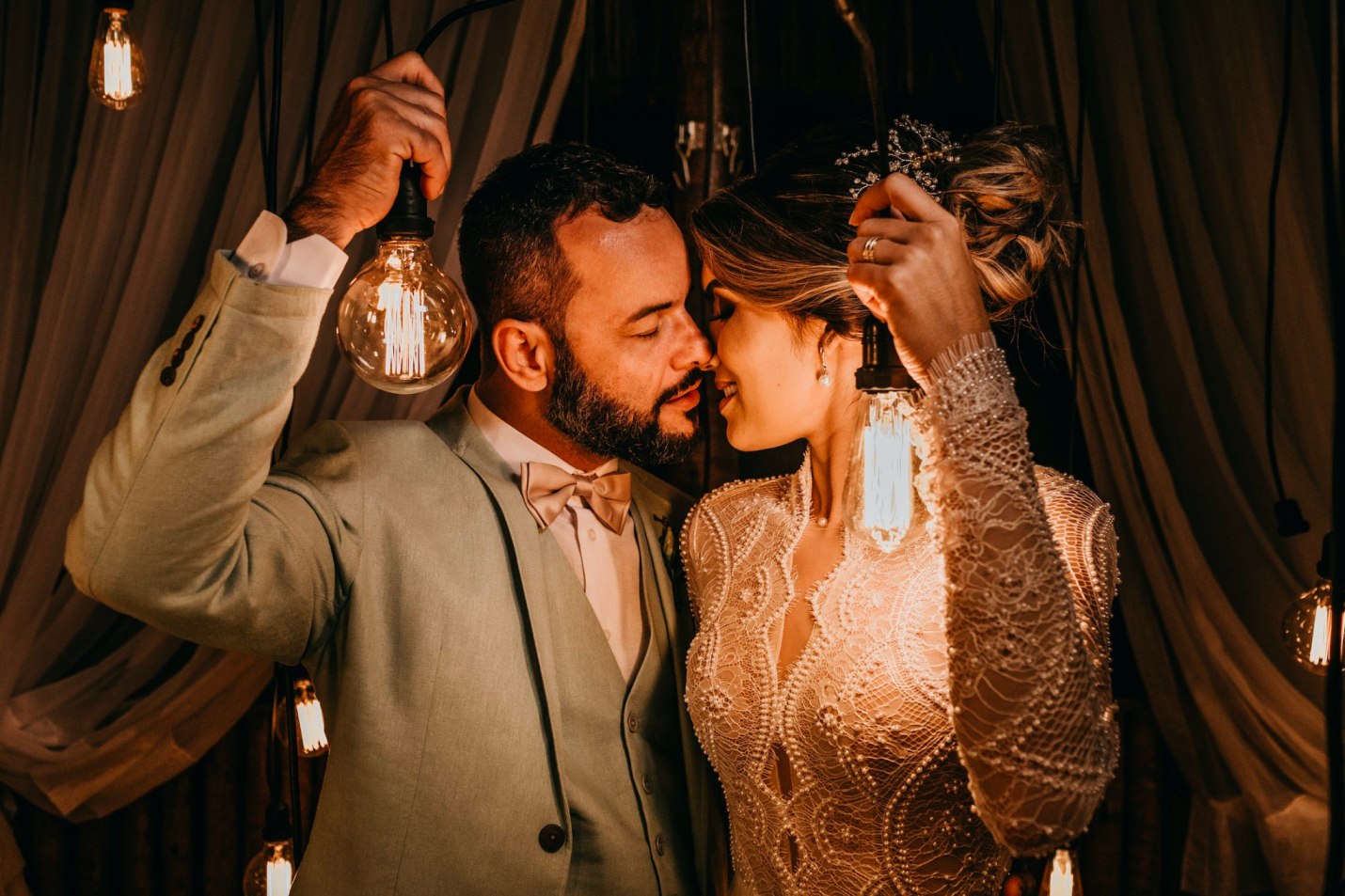 A bride and groom hold bistro lights while smiling and posing for a kiss
