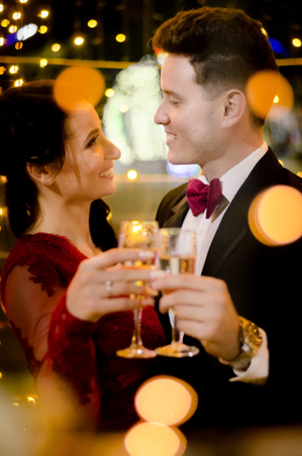 couple holding champagne glasses at their engagement with warm lights