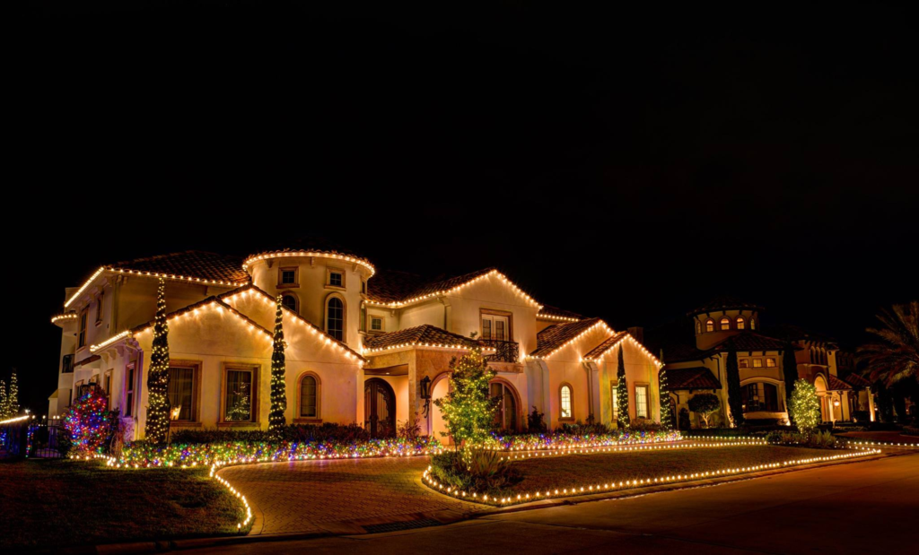 A large luxury home beautifully outlined with warm holiday lights glowing against the night sky.