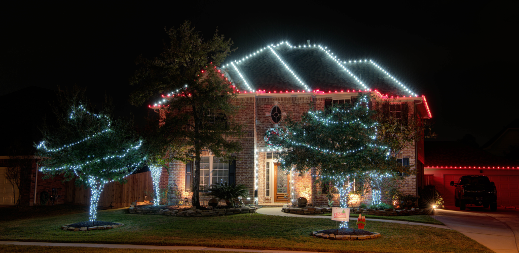A brick house at night, decorated with festive red and white lights outlining the roof and wrapped around trees in the front yard.